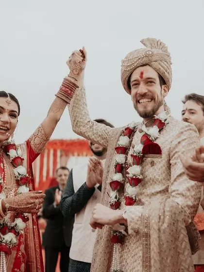 A moment of pure triumph and joy. The couple celebrates after their varmala exchange, their hands raised in happiness, surrounded by their cheering family and friends.