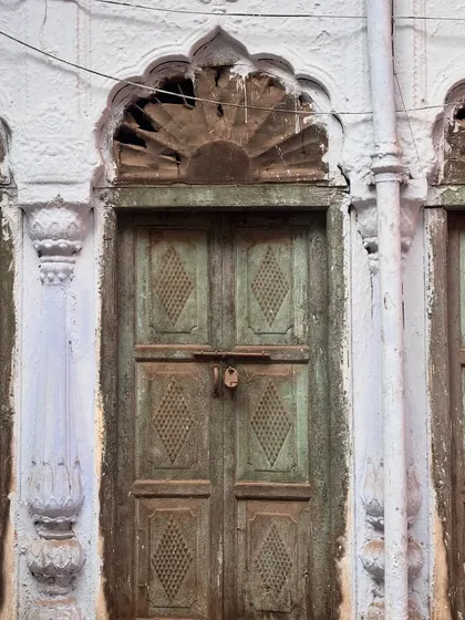 A weathered green door with a sunburst arch, showing signs of decay but still retaining its elegant form. Each haveli tells a story of time, weather, and changing fortunes.