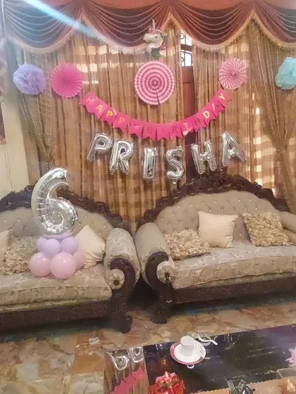 A birthday setup in a living room for Prisha's 6th birthday. The decor includes a "Happy Birthday" banner, name foil letters, and a number "6" foil balloon.