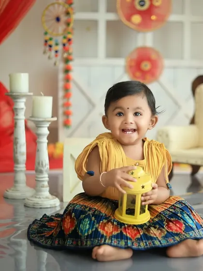 A beautiful, smiling toddler holding a lantern in our vibrant Diwali setup. Her traditional dress and the festive decor create a stunning cultural portrait.