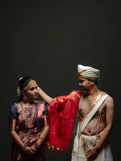 A modern, minimalist portrait of a couple in traditional South Indian attire. The clean background and simple posing highlight their connection and the beauty of their outfits.