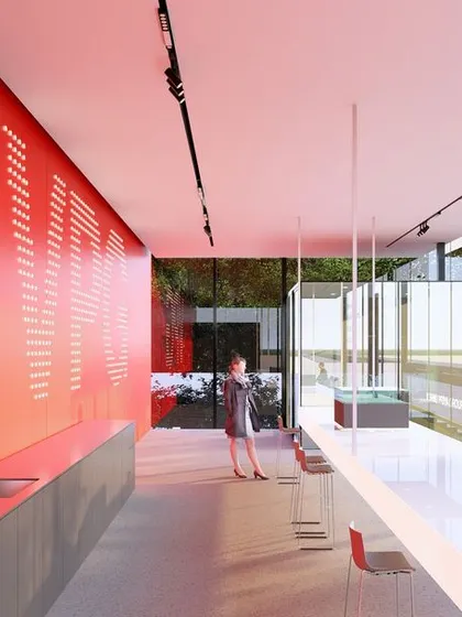 The interior of the real estate experience center. A bold red wall contrasts with the minimalist white and glass surfaces, creating a dynamic and memorable space for customers.