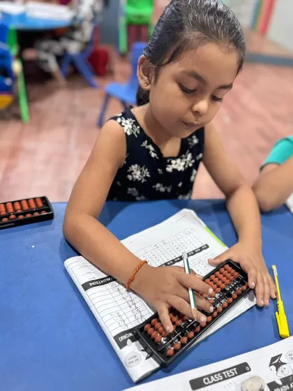This young girl is carefully moving the beads on her abacus. This tactile learning process is the first step towards mastering mental math and is perfect for young learners.