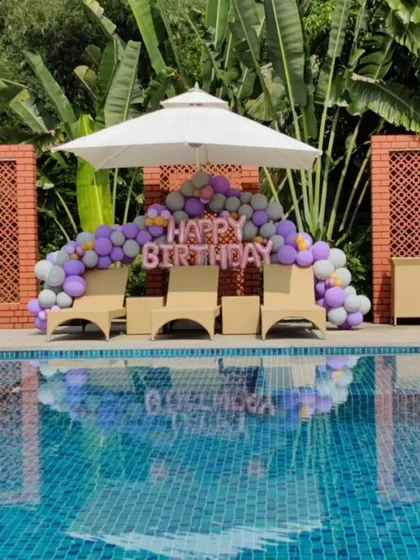We can decorate any space, even by the pool. This poolside birthday setup features a balloon garland in purple and grey with 'Happy Birthday' foil letters, creating a fun and festive vibe.