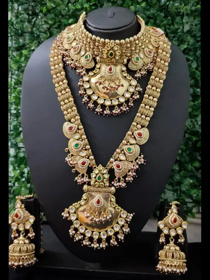 This is a classic example of my traditional temple jewellery collection available for rent. The set features a statement choker and a long necklace with antique gold finishing, detailed with motifs and colored stones, complete with heavy matching jhumkas. It’s perfect for achieving a timeless South Indian bridal look.