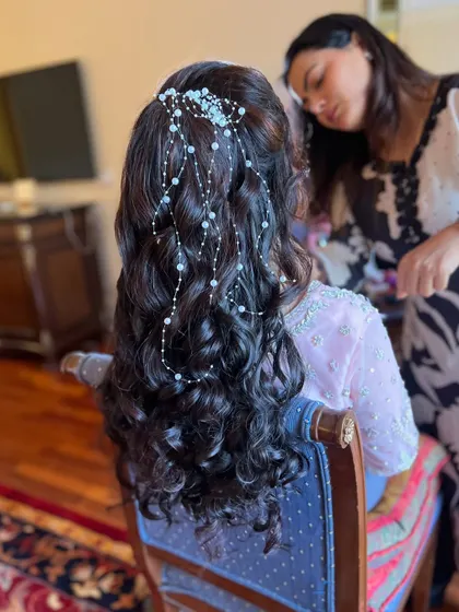 A beautiful half-up style with soft curls and a cascading pearl accessory. This behind-the-scenes shot shows the final touches being made.