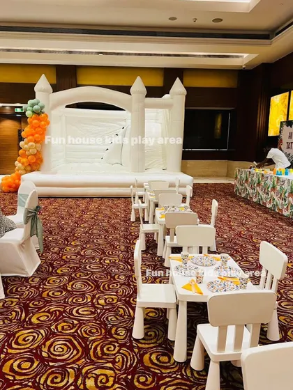 A full event view with our large white bounce castle as the main attraction, complemented by kids' dining tables for a complete party setup.