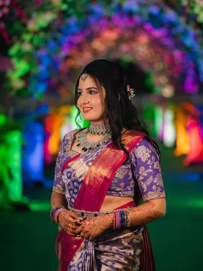 A client looking gorgeous at her reception in a purple saree, paired with a modern diamond-look necklace with green stones.