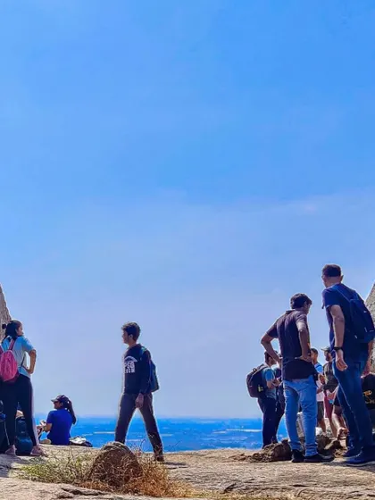 A group of trekkers resting and enjoying the view at Nijagal Betta, with the sky and horizon blending into a beautiful blue.