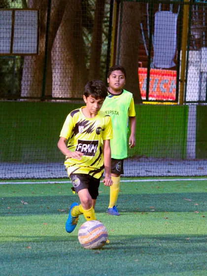 A player dribbles with focus and determination, with a teammate watching in the background. This highlights the individual skill within a team context.