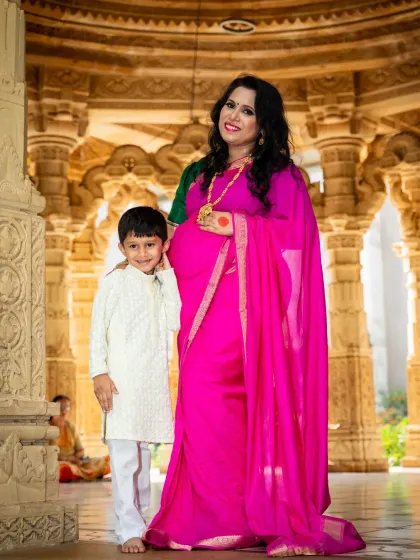 A beautiful maternity portrait taken in a traditional setting. The mother-to-be, dressed in a vibrant pink saree, stands with her son, creating a culturally rich and graceful image.
