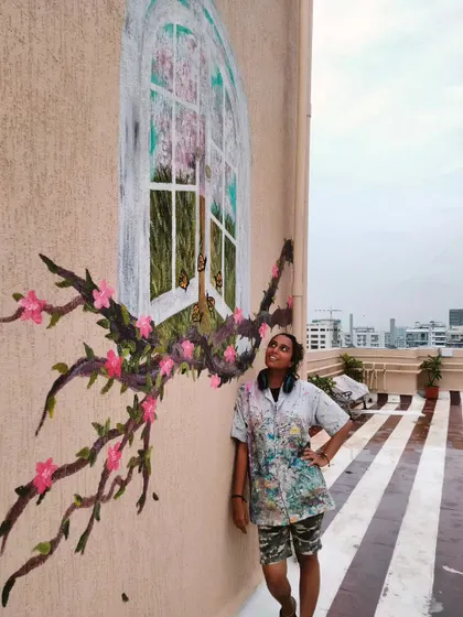 Guess I said yes to heaven. Me looking up at a finished terrace mural that features a whimsical window opening to a world of blossoms, with flowering branches wrapping around it.