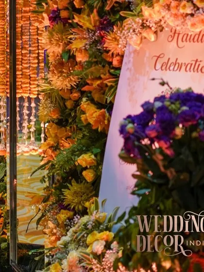 The welcome signage for the Haldi celebration, nestled within a lush floral arrangement. The warm lighting makes the sign glow, creating an inviting entrance.