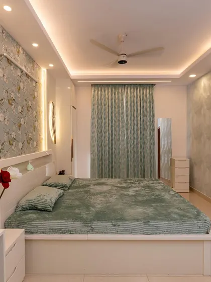 The master bedroom is a breath of fresh air, with a floral wallpaper accent wall, soft green tones, and elegant ceiling lighting that creates a restful atmosphere.