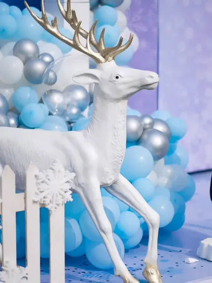 A close-up of a majestic white reindeer prop with golden antlers, set against a backdrop of blue and silver balloons.