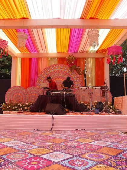 A Haldi is incomplete without music. The performance stage was designed to match the event's vibrant theme, with a colorful patterned backdrop, striped drapes, and fun hanging lamps.