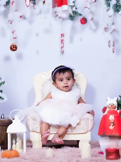 A festive Christmas portrait in the studio. The little girl is dressed in white, surrounded by miniature Christmas trees and decorations, creating a perfect holiday card photo.