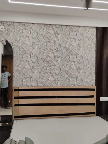 A modern bedroom with a leaf-patterned wallpaper behind the headboard, integrated with wood paneling and accent lighting for a high-end look.
