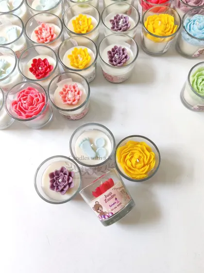 An assortment of votive jar candles with various toppers like peony flowers, baby feet, and succulents, perfect for a first birthday.