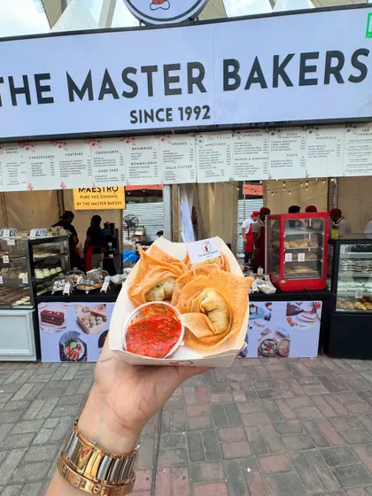 A customer holding a fresh serving of our crispy fried wontons at our outdoor stall. These golden pockets are filled with a savory vegetable mix and served with a tangy dipping sauce, perfect for a quick and satisfying snack.