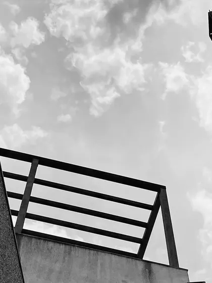 A black and white detail of the pergola structure at Ridge House under construction, framed against a cloudy sky.