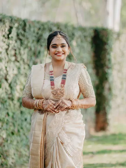 A smiling portrait of our client, showcasing her beautiful ivory-gold ensemble. The intricate detailing on her blouse and her traditional jewelry come together to create a look of timeless elegance.