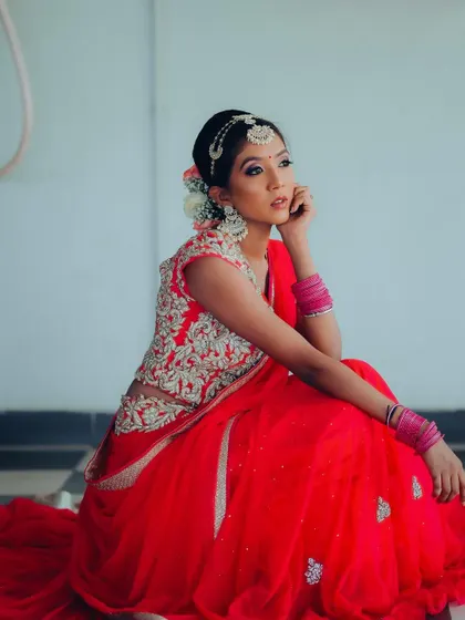 A beautiful portrait of a bride in a vibrant red lehenga. The seated pose allows the full skirt to spread out, creating a dramatic and elegant effect.