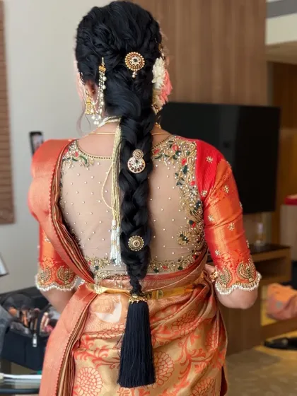 A detailed shot of a textured bridal braid adorned with traditional gold accessories and a black tassel (kunjalam) at the end.