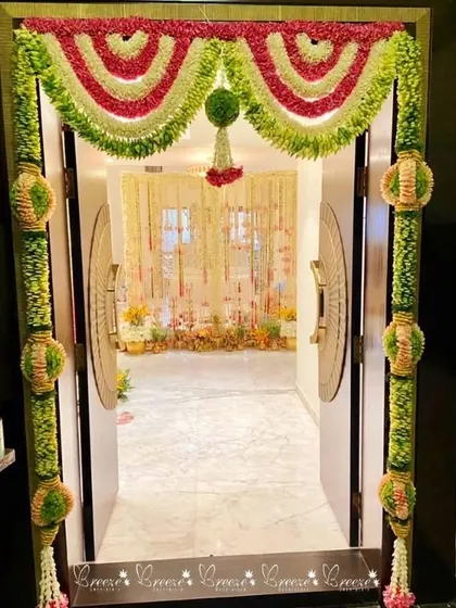 This is a traditional floral entrance for a home event. The doorway is framed with intricate garlands made of fresh flowers and green leaves, setting a festive tone right from the start.