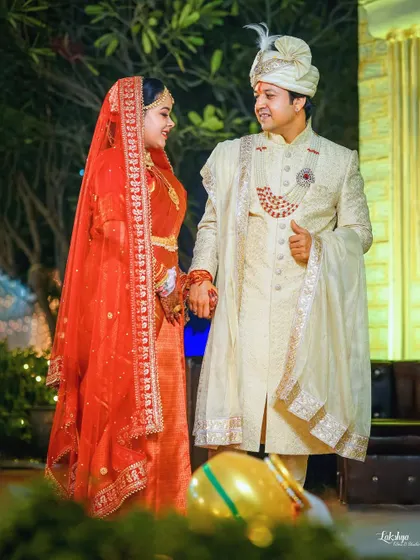 A lovely full-length portrait of the couple in an outdoor setting. Their classic red and white outfits stand out beautifully against the natural greenery.