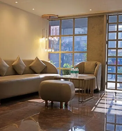 The waiting lounge of a hotel project, designed to be a calm and welcoming first impression. The space uses a neutral color palette, a gracefully curved sofa, and industrial-style gridded windows that allow natural light to flood the polished floor.