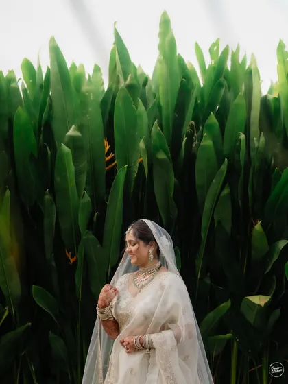 A quiet, candid portrait of the bride against a wall of large green leaves, creating a natural and serene frame.