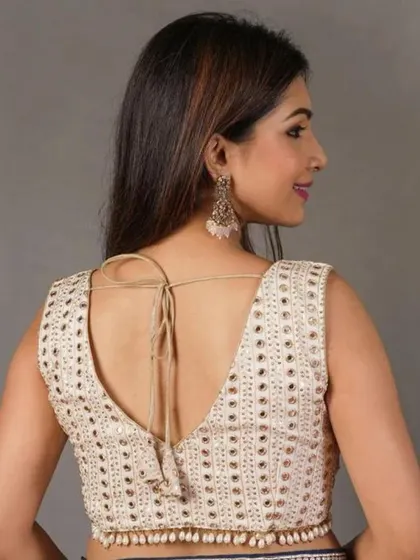 This off-white blouse features a V-back with a tie-up tassel. The fabric is covered in intricate mirror work, adding a touch of sparkle.