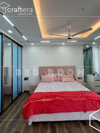 This bedroom features a soft pink upholstered bed and a sliding wardrobe with mirrored panels that enhance the sense of space. The track lighting on the ceiling adds a modern touch.