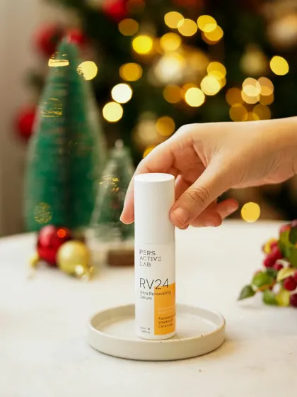A hand holds the serum in front of a festive, bokeh-lit background. This product-focused shot uses soft, warm lighting to create a magical, celebratory mood perfect for a holiday campaign.