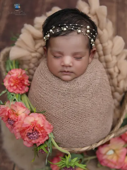 This baby is swaddled in a neutral brown wrap and placed in a rustic basket. The addition of fresh pink flowers adds a soft pop of color to the earthy tones.