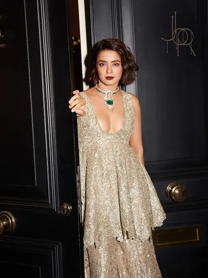 A full shot of Surveen Chawla in a glittering gown, her look anchored by the magnificent emerald centerpiece necklace.