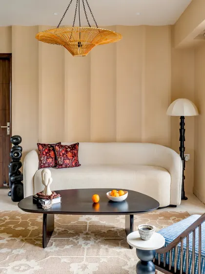 A full view of the 'Project Lily' living room, highlighting the blend of textures and earthy tones. The space is furnished with a custom sofa, a unique totem-pole-style floor lamp, and a patterned rug.