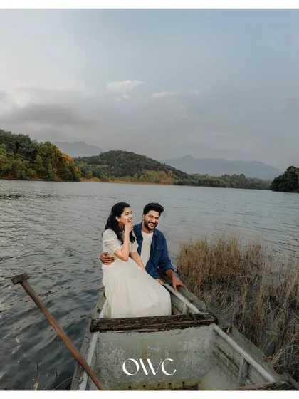 A stunning wide shot of a couple in a boat on a lake, surrounded by mountains, creating a breathtaking pre-wedding landscape.