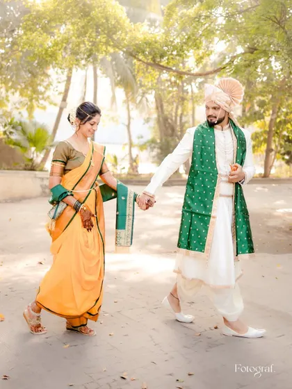 A Marathi couple in traditional attire, walking hand-in-hand with a playful energy. The groom leads his bride with a smile.