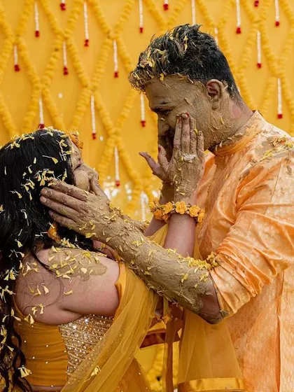 A candid moment of a couple 'Haldified'. The backdrop of yellow marigold strings creates a classic, vibrant setting for this joyful ritual.