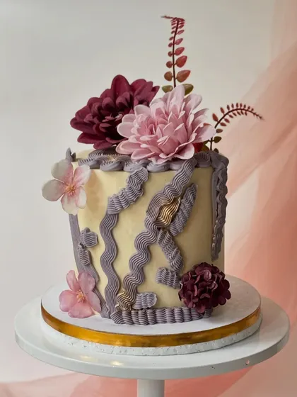 A modern cake with abstract purple piping and textures. The design is finished with a mix of purple and pink silk flowers for a contemporary floral look.