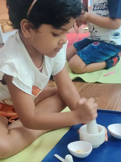 A child is completely absorbed in her work with a mortar and pestle. This activity strengthens her hands and wrists while providing a satisfying sensory experience of grinding spices or grains.
