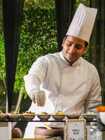 A chef at our Pomelo Salad station, adding a final garnish with a smile. Our live salad bars offer a fresh and healthy option, customized to each guest's preference.