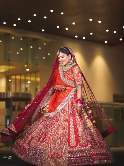 A joyful, twirling bride. This full-length portrait under a ceiling of lights captures her happiness and the beautiful movement of her orange and red lehenga.
