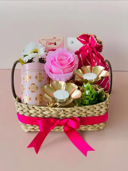 This Kauna basket with a handle is curated with a pink and gold theme, featuring a printed tin, golden t-light holders, and a decorative rose.