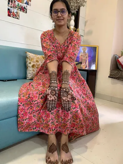 A happy client showing her complete mehndi set, including designs on her hands and feet. The foot design is a simple yet elegant mandala that matches her hand patterns.