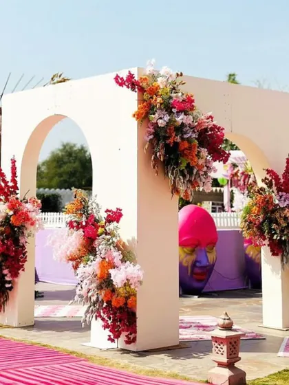 A modern, minimalist archway decorated with vibrant floral arrangements, serving as a photo point for a colorful carnival event.