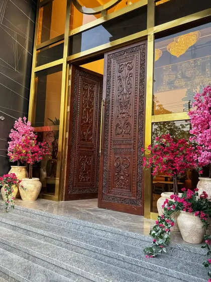 A wider view of the grand entrance, flanked by our beautiful faux floral arrangements. The vibrant pinks pop against the dark marble and intricately carved wooden doors.