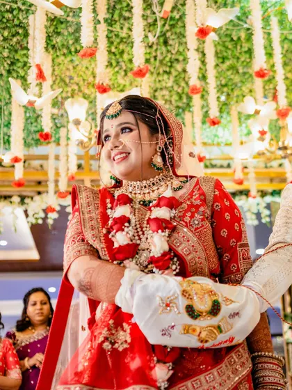 The bride's joyful smile during the Pheras ceremony. Dressed in a stunning red lehenga and surrounded by floral decor, this image captures the happiness and sanctity of the moment.